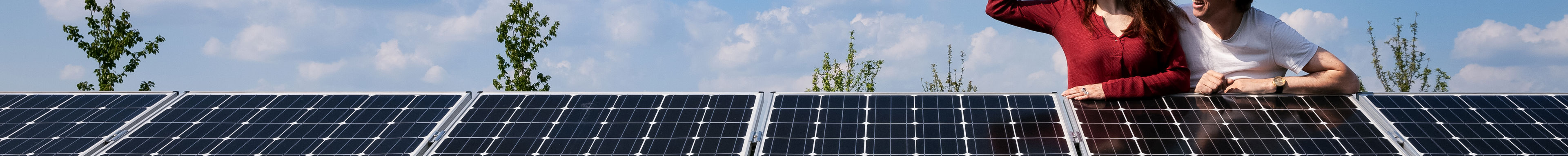 Twee mensen leunen over een rij zonnepanelen en kijken samen naar links
