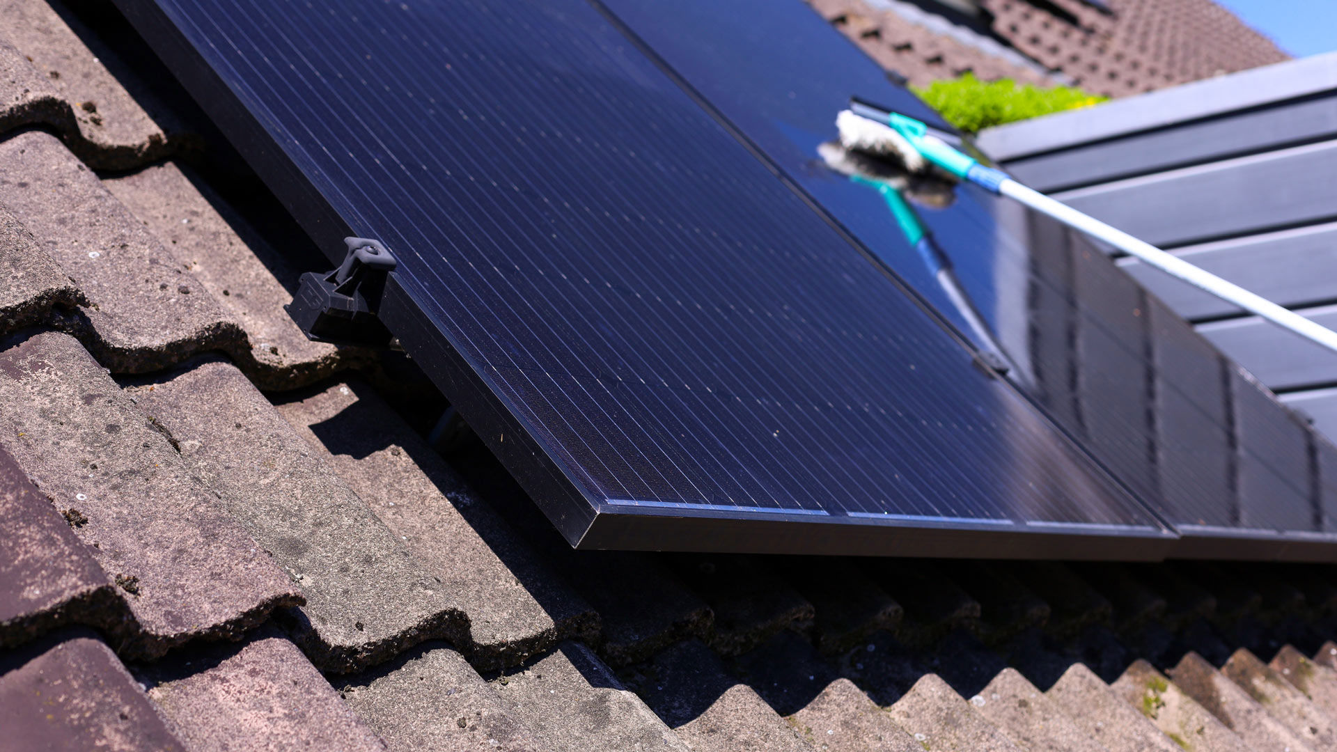 Close-up van zonnepaneel op een schuin dak. In de achtergrond wordt het paneel schoongemaakt.